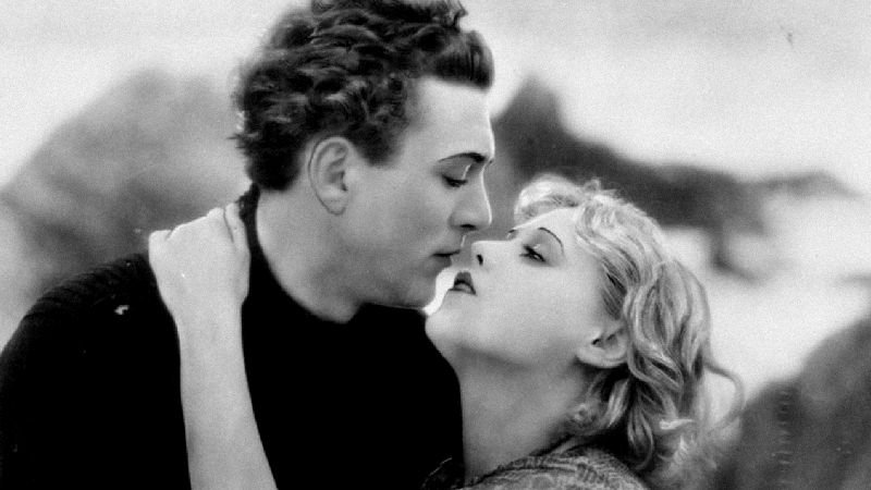 A black and white film still showing a man and a woman in a romantic embrace.